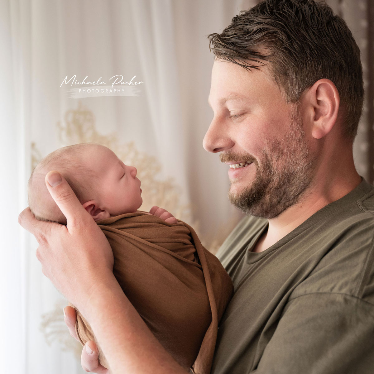 Vater hält sein neugeborenes Baby liebevoll im Arm und blickt lächelnd auf das schlafende Kind.